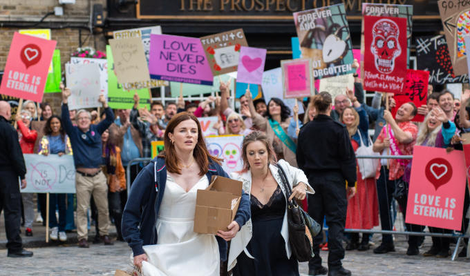 Aisling in front of crowd with placards saying things like Love Is Eternal